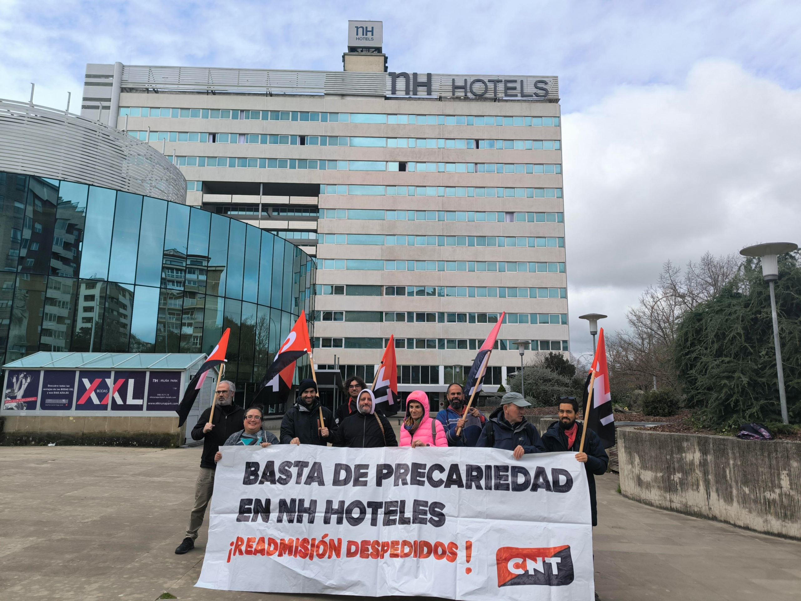Compañeras de CNT Iruñea se concentran ante NH Hoteles. Sostienen una pancarta donde se puede leer "Basta de precariedad en NH Hoteles. ¡Readmisión despedidos!" y el logo de CNT.