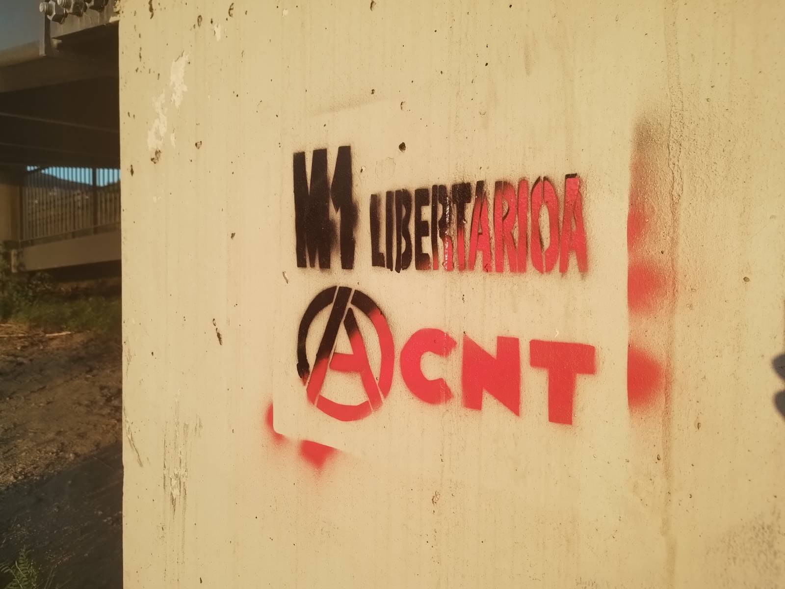 Horma baten gainean pintada gorri-beltza. Hau irakur daiteke: M1 Libertarioa. Azpian, anarkiaren A letra eta CNTren logo klasikoa.
